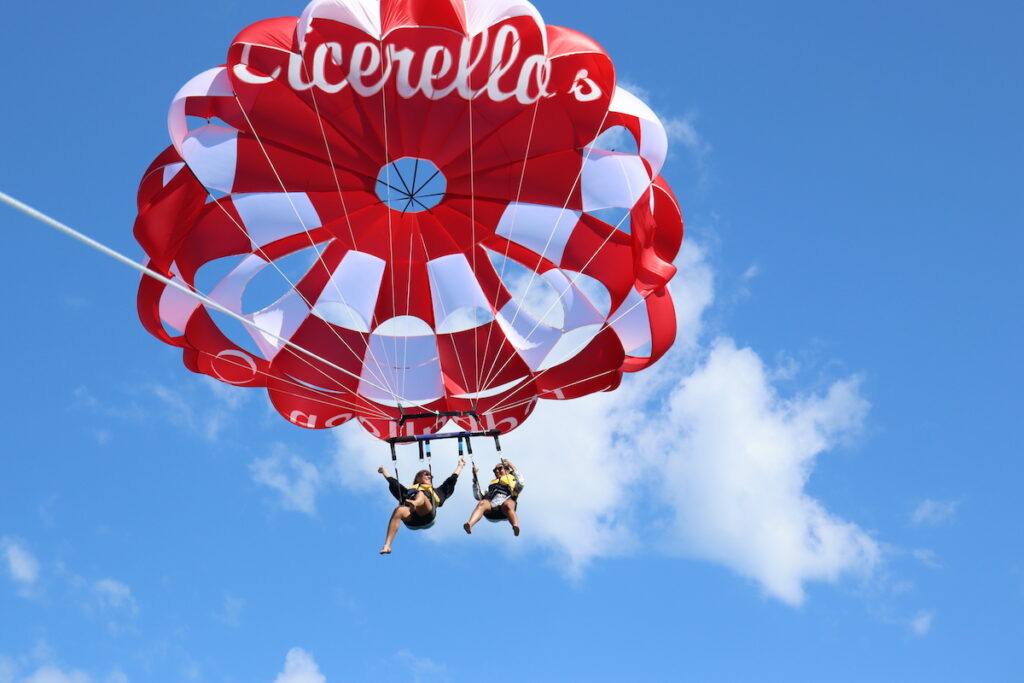 Two people suspended under a red and white parachute, parasailing.